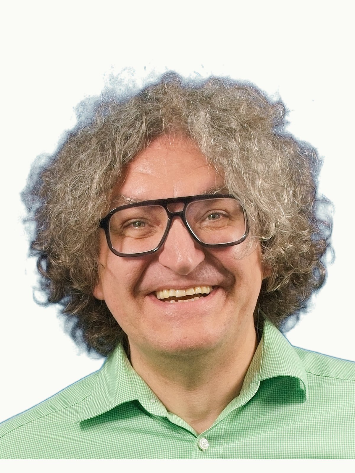 Portrait von Eike Totter. Volles, lockiges Haar, ikonische Brille, direkter Blick, heller Hintergrund.